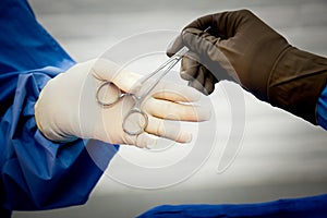 Surgeon`s hand in white latex glove being handed a hemostat by doctor in brown latex glove