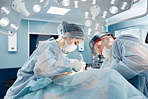 Surgeons in a light operating room perform plastic surgery, a team of male and female doctors perform reconstructive