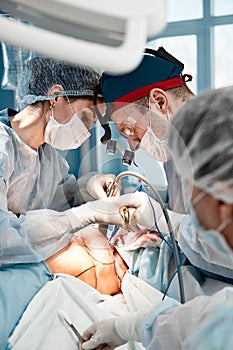 Surgeons men and women in one team during an operation over the operating table, doctors in modern equipment perform an