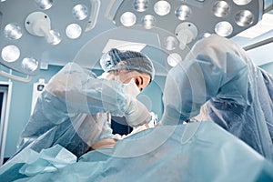 Surgeons men and women in one team during an operation over the operating table, doctors in modern equipment perform an