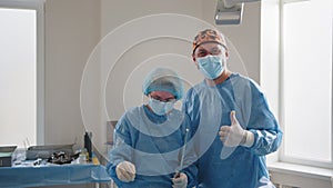 Surgery, medicine and people concept - group of surgeons in operating room at hospital showing thumbs up. Doctors in