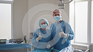 Surgery, medicine and people concept - group of surgeons in operating room at hospital showing thumbs up. Group of
