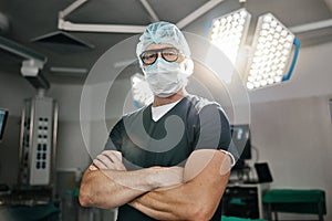 Surgery, portrait and arms crossed by man doctor in operating room with confidence in medical, healthcare or emergency