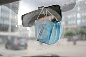 Surgical face mask as protection against covid-19 infection is hanging in a car on the rear view mirror during the coronavirus