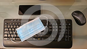 Surgical face protection mask on a keyboard near smartphone and a mouse