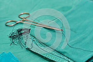 A surgical holder and needle with silk on green cloth