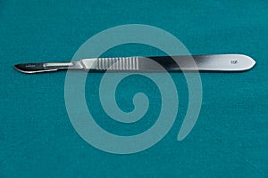 Surgical instrument, stainless steel scalpel handle number 3 with blade number 10 isolated on surgical green drape