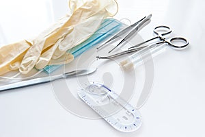 Surgical instruments forceps for closing a wound, curved tweezers, thread with needle, medical mask and rubber gloves on white bac