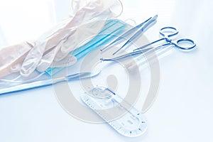 Surgical instruments, forceps to close the wound, curved tweezers, thread with needle, medical mask and rubber gloves on a white b