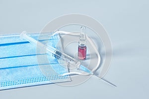 Surgical mask for cover mouth and nose and red vaccine, syringe on gray background