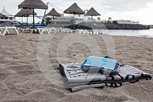 Surgical mask on flip flops and a towel on the beach, new normality on the beach, social distancing and protective mask