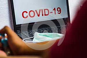 Surgical mask on a laptop keyboard that reads covid-19 on the screen
