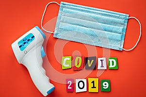 Surgical medical mask for protection from virus, infrared non contact thermometer for measuring temperature, COVID-19 text.