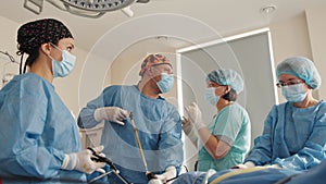 Surgical Team Working In Operating Theatre. During the operation in the operating room, a nurse or assistant fixes the