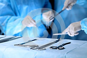Surgical tools lying on the table while group of surgeons at background operating patient. Steel medical instruments