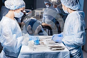 Surgical tools lying on table with nurse near and surgeons at background.