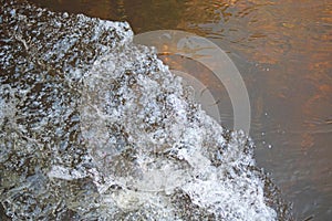 SURGING WHITE FROTH SPILLING INTO WATER WITH AMBER COLOURED BOTTOM