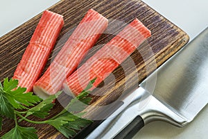 Surimi crab sticks on a brown cutting board near a sharp chef knife. Seafood and ingredient for salads. Healthy eating and cook at