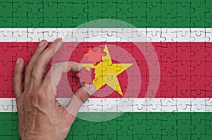 Suriname flag is depicted on a puzzle, which the man`s hand completes to fold