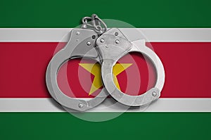 Suriname flag and police handcuffs. The concept of observance of the law in the country and protection from crime