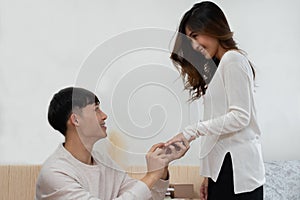 A surprise Asian couple proposes to marry. Young man kneeling and wearing a ring on his girlfriend finger