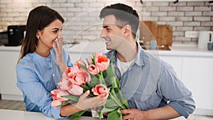 Surprise! Beautiful romantic couple at home. A young man gives flowers to his beloved. A feeling of happiness. Pink tulips