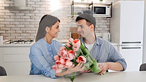 Surprise! Beautiful romantic couple at home. Young man is presenting flowers to his beloved. Feel of happiness