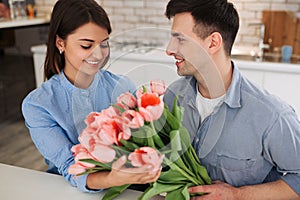 Surprise! Beautiful romantic couple at home. Young man is presenting flowers to his beloved. Feel of happiness