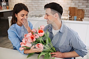 Surprise! Beautiful romantic couple at home. Young man is presenting flowers to his beloved. Feel of happiness