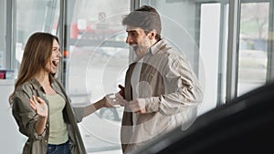 Surprise gift. Young excited woman opening her husband eyes at car dealership center, young amazed guy enjoying present
