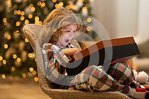 Surprise kid opening Christmas magic presents. Happy excited child open Christmas gift near christmas tree at home.