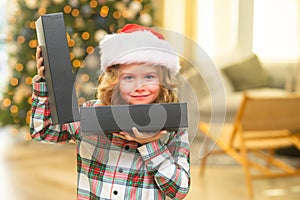 Surprise kid opening Christmas present gift box. Happy funny child in Santa hat holding Christmas gift. Christmas and