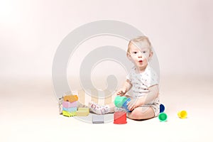 Surprised adorable baby boy sitting on the floor and playing with his toys.