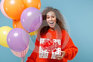 Surprised african american girl in orange knitted clothes isolated on blue background. Birthday holiday party concept