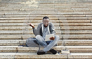 Surprised african-american student sitting on stairs using digital tablet