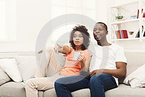 Surprised african-american young couple watching TV at home