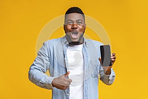 Surprised african man holding smartphone and showing thumb up