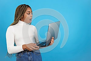 Surprised african woman standing holding a laptop