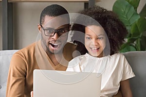 Surprised amazed black dad and kid daughter looking at laptop