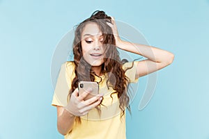 Surprised and amazed young woman using phone isolated over the blue background. Good news concept.