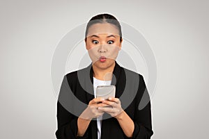 Surprised Asian businesswoman in a black blazer looking at her smartphone with an exaggerated expression of shock