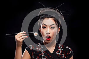 Surprised Asian woman eating sushi and rolls on a black background.