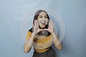 Surprised Asian woman reclines on her hands and shouting while looking at the camera over blue background