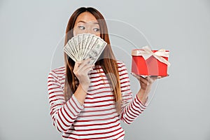 Surprised asian woman in sweater hiding behind a money