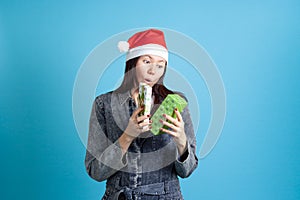 surprised Asian young woman in a Santa Claus hat looks into an open gift box, on a blue background