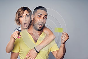 Surprised astonished couple showing blank credit card and pointing at you
