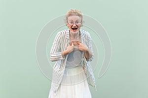 Surprised astonished excited woman wearing striped shirt and skirt, pointing at herself being amazed