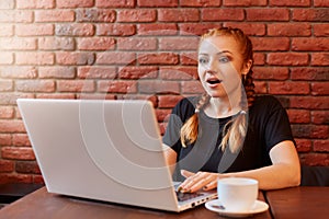 Surprised astonished young woman with red hair and two pigtails, sitting with open mouth, being in amazement, shocked by