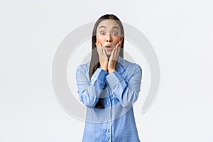 Surprised and astounded beautiful asian girl react to wonderful unexpected news, looking amazed with hands over face and