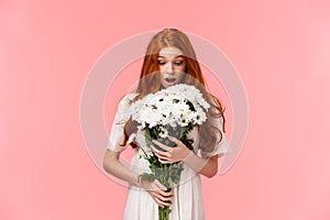 Surprised attractive redhead girl receive romantic valentines day gift, looking at beautiful bouquet of flowers amazed